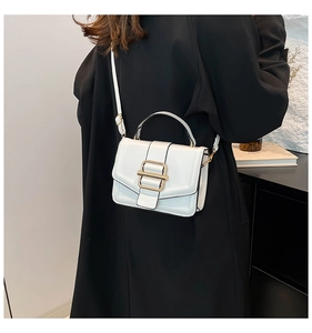 Close-up of a glossy white handbag with a gold metal buckle on a black coat outfit
