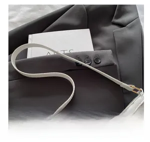 Macro shot of white leather bag with gold bow buckle and slim shoulder strap detail