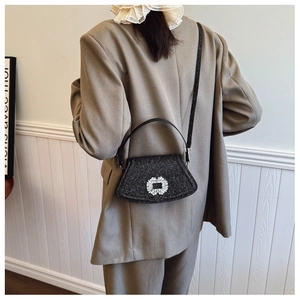 Détail d'un sac à bandoulière en paillettes noires avec boucle strass porté par un mannequin