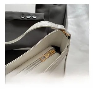 Detail view of smooth golden metal zipper on a premium white leather crescent bag
