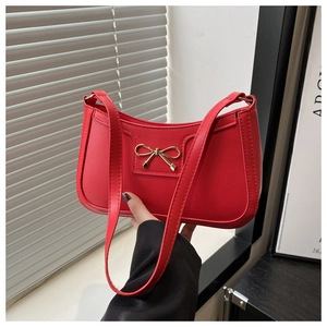 Detail of red crescent bag with gold bow hardware and shiny synthetic leather finish