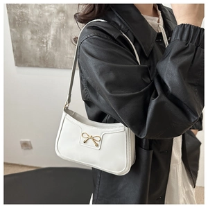 Close-up of white crescent shoulder bag featuring elegant golden bow metal hardware detail