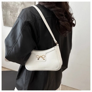 Detailed shot of a white crescent bag featuring a golden metal bow and precise stitching