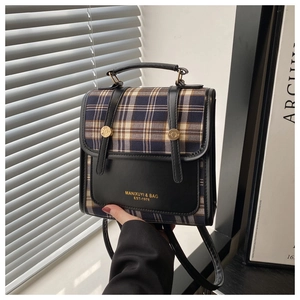 Detailansicht der Vintage-Karo-Klappe und Goldlogo auf dem schwarzen Lederrucksack