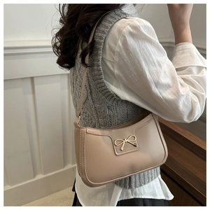 Beige crescent underarm bag with golden bow detail shown on a model for scale