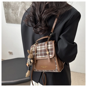 Detail of vintage plaid mini backpack featuring gold logo and cute plush rabbit charm