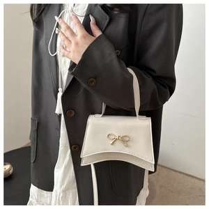 Detail of a creamy white mini handbag featuring a golden bow metal accessory on matte leather