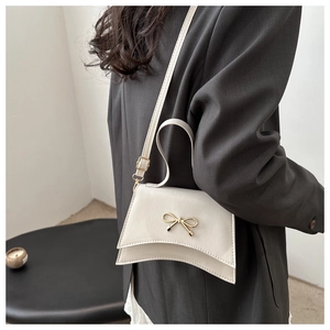Detail view of cream crossbody bag featuring a golden bow and unique curved base design