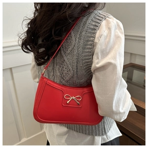 Detail of red matte shoulder bag featuring a gold bow clasp and elegant curved base