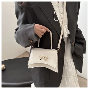 Detailed view of white crossbody bag with golden bow and elegant matte leather texture