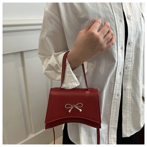 Detail of red crossbody bag featuring a golden bow buckle and smooth leather finish