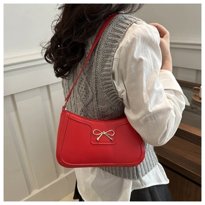 Detail of red leather crescent bag with golden bow buckle worn by a model