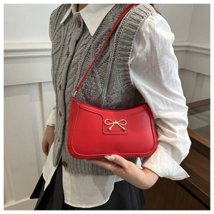 Close-up of red crescent bag featuring a delicate gold metal bow accent and faux leather texture