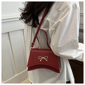 Detail of red crossbody bag with metal bow and curved bottom on white shirt background