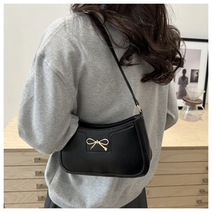 Detail of black crescent shoulder bag with a gold metal bow on a model's shoulder