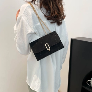Stylish black shoulder bag with gold chain strap and buckle shown on a model