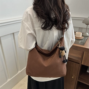 Brown canvas hobo bag with plush sheep pendant worn by a model in a minimalist room