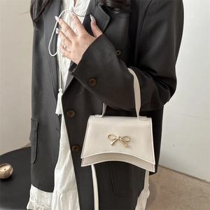 Chic cream crossbody bag with golden bow accent and wavy side detail for women