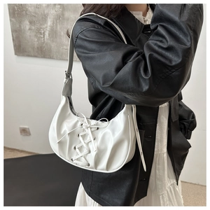 Detail view of a white crescent shoulder bag with lace-up ties worn by a model