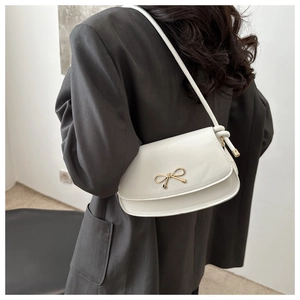 Détail du sac sous le bras en cuir verni blanc avec décoration nœud doré en métal