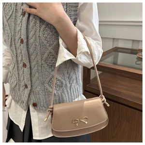 Détail d'un sac à bandoulière en cuir beige avec nœud doré et fine bandoulière