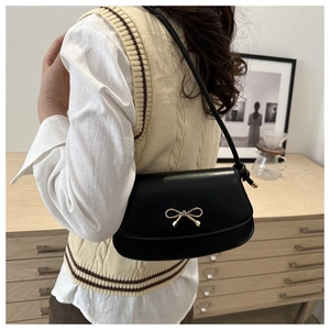Elegant black leather baguette bag with a gold bow buckle worn by a model in a cozy room