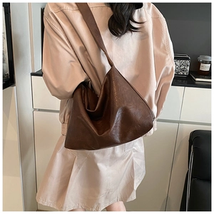 Rear view of a large brown leather hobo bag with wide shoulder strap on a model