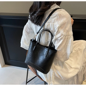 Close-up of black leather bucket bag featuring a gold buckle and embossed fashion logo