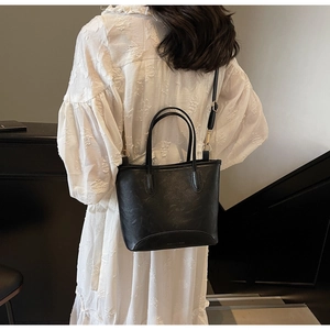 Minimalist black bucket bag with slim handles and gold hardware on white dress
