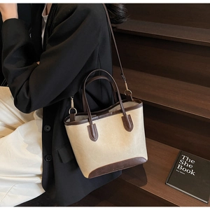 Detail of beige and brown bucket bag showing metal side buckles and leather textures