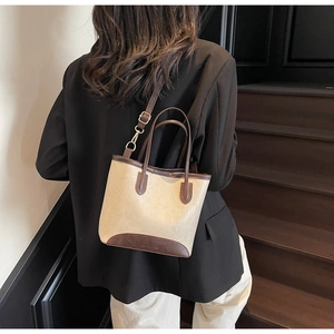 Detail of beige and brown bucket bag with gold hardware shown on a black suit