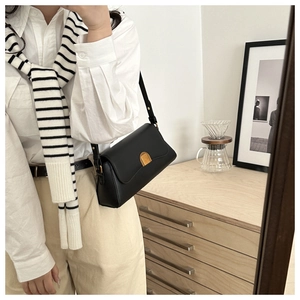 Detail shot of black minimalist leather baguette bag with golden metal clasp in a lifestyle setting