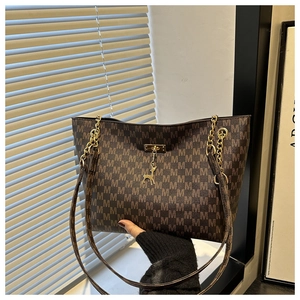 Detail of brown tote bag with M-pattern, gold chain strap and deer charm pendant