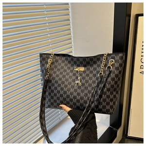 Detail of black tote bag with M-pattern print, gold chain strap, and deer charm