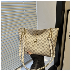 Detail of cream tote bag with M-letter jacquard, gold chain, and deer pendant
