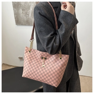 Detail of pink tote bag with M-pattern, gold chain strap, and deer pendant on grey coat