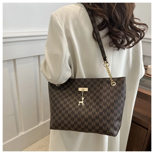 Detail of brown tote bag featuring M-letter print and golden deer charm on chain strap