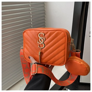 Close-up of orange quilted camera bag with gold logo, wide strap, and round coin purse