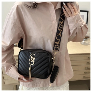 Detail of black quilted crossbody bag with wide jacquard strap and gold tassel