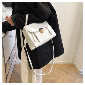 Detail of elegant white crossbody bag with gold hardware worn by a model in casual setting