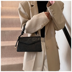 Detail of vintage black handbag with embossed floral and koi fish patterns on a beige suit