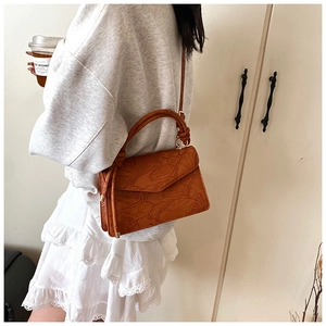 Detail of vintage embossed floral pattern on a tan crossbody bag with tassel accent