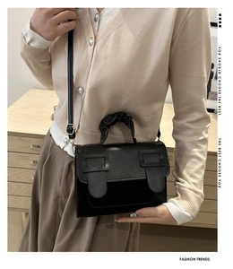 Detail of black crossbody bag with ruched handle and dual buckle design on model