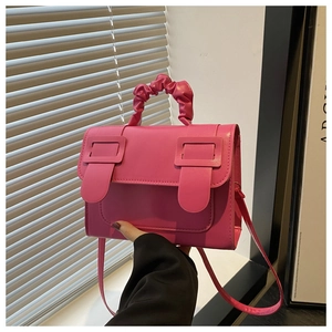 Close-up of fuchsia crossbody bag featuring a pleated handle and large square buckle detail