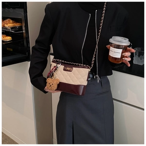 Détail d'un sac seau matelassé beige avec cuir bordeaux et breloque petit ourson
