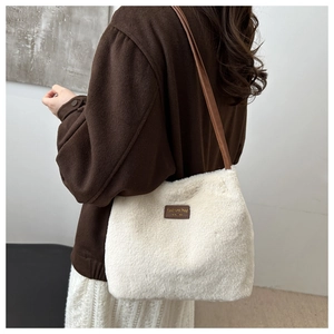 Détail du sac seau en peluche blanc cassé avec bandoulière en cuir brun et étiquette logo
