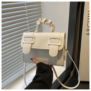 Detail of white textured leather crossbody bag with pleated handle and metal buckles