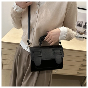 Detail of black leather crossbody bag with pleated handle and metal buckle accents