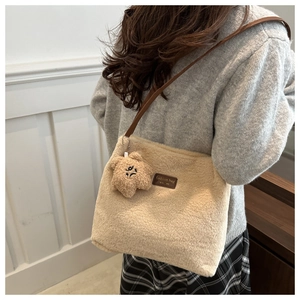 Détail d'un sac cabas en peluche beige avec lanières en cuir marron et breloque ours