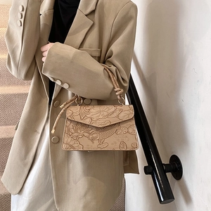 Retro light brown embossed handbag with lotus and koi patterns worn by model in warm light